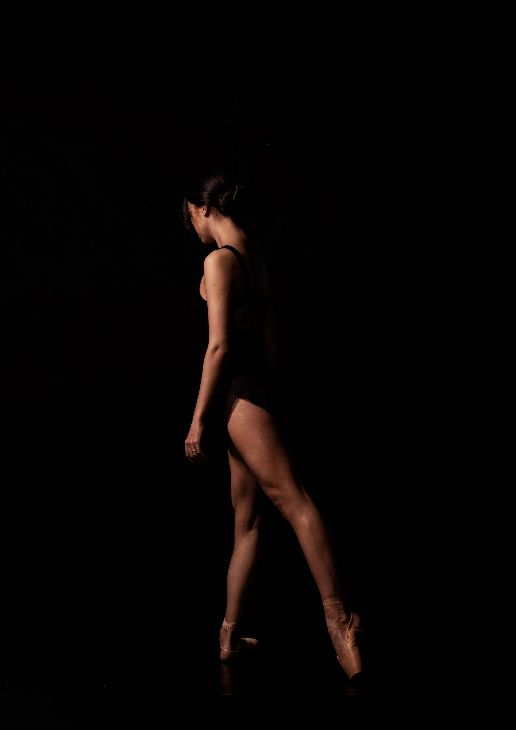 Ballerina di profilo sulle punte, isolata nel buio