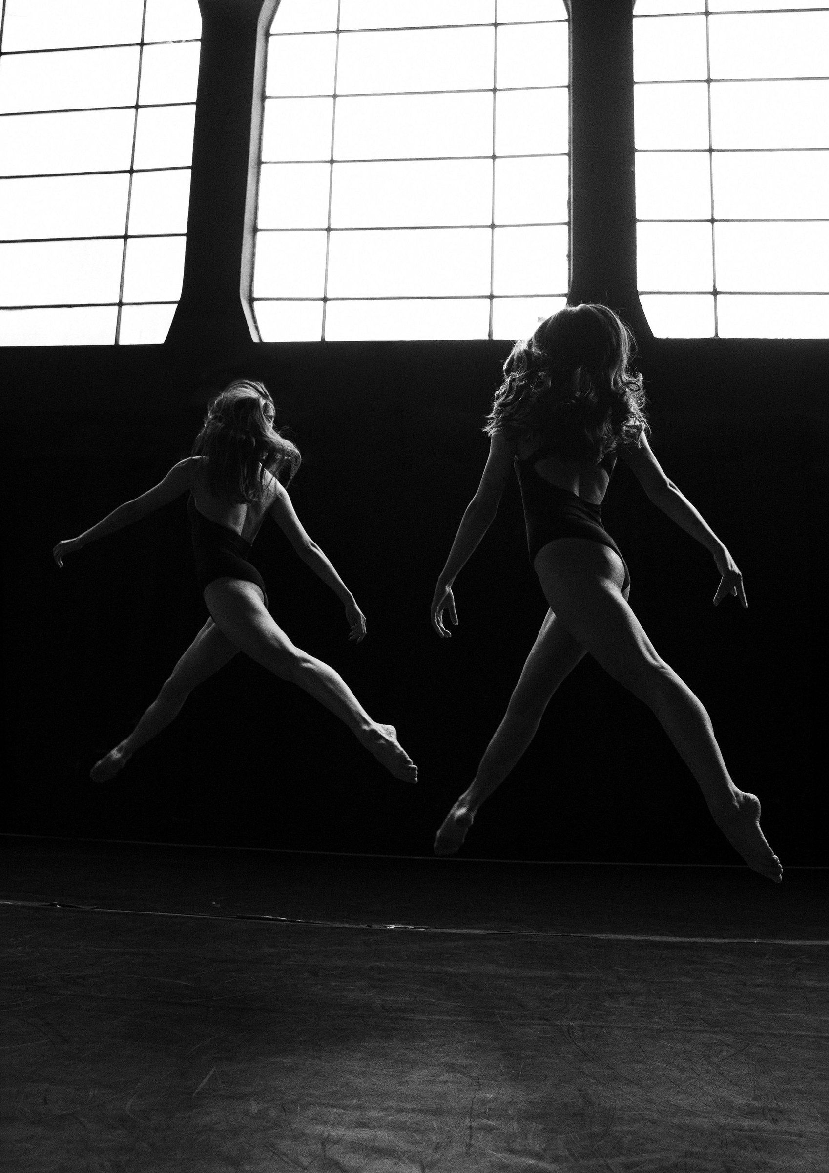 Bianco e nero: due ballerine saltano davanti alle finestre della sala prove