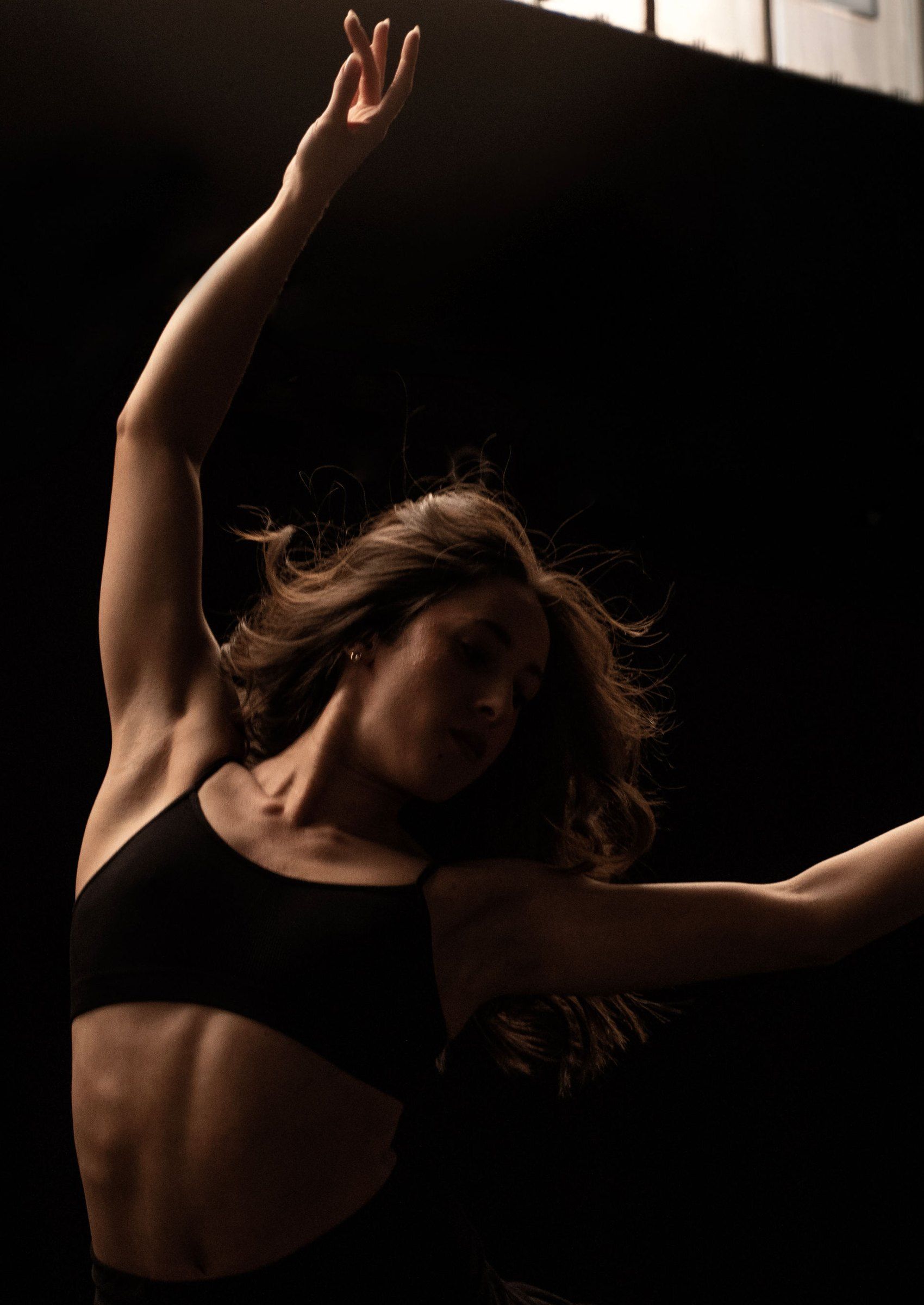 Ballerina con un braccio alzato, l’addome nella luce